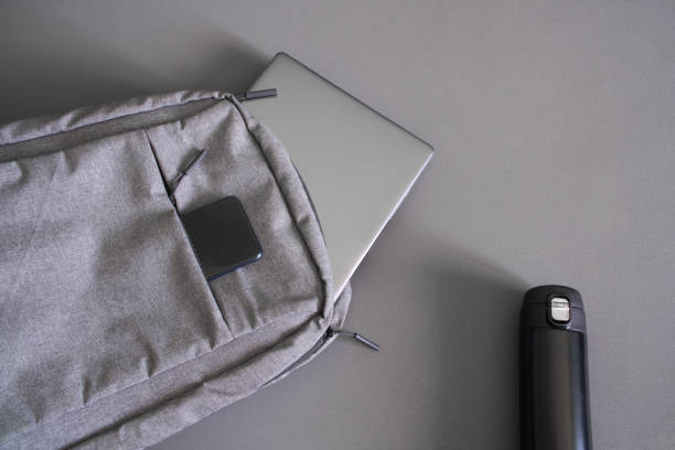 istock Small textile urban backpack with a gray laptop or ultrabook, a smartphone and a small camping thermos. Gray background. Traveling with gadgets. Copy space 1404944952