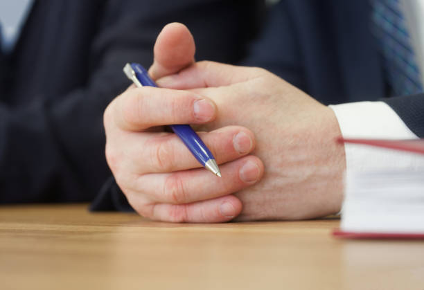 Folded hands of politician, deputy or businessman on the table along with pen. Official, boss, lawyer or delegate. Participation in negotiations. Copy space. No face Folded hands of politician, deputy or businessman on the table along with pen. Official, boss, lawyer or delegate. Participation in negotiations. Copy space. No face. Close-up procedural generation stock pictures, royalty-free photos & images