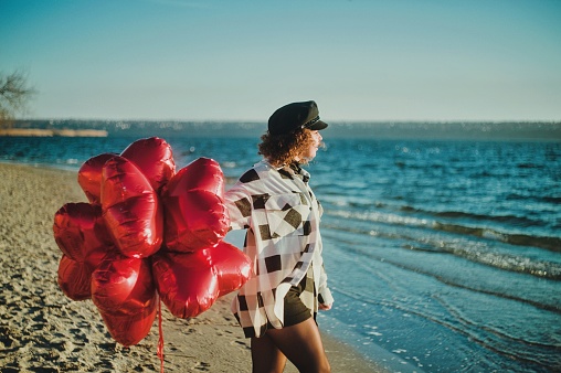 Young woman with a red heart balloons runing on the beach