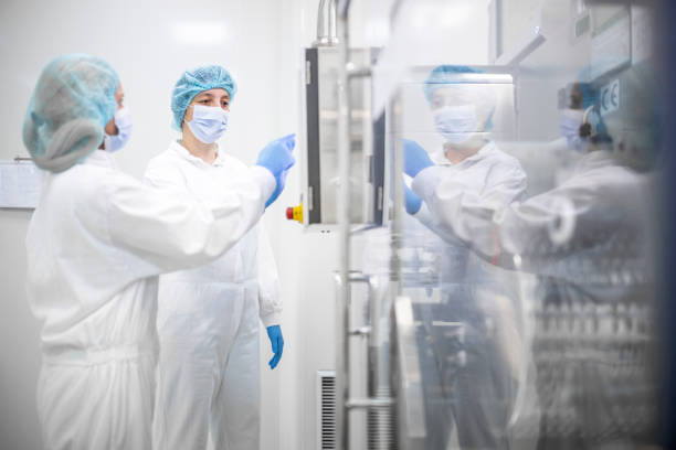 istock Female employees in a pharmaceutical laboratory  wearing proper equipment seen while pushing a button on the machine in a laboratory during pharmaceutical manufacturing 1404945060