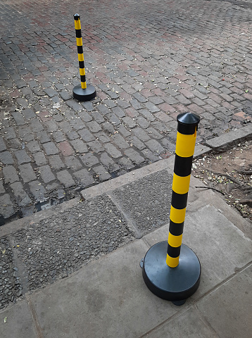 Yellow and black signaling pylon on cement sidewalk