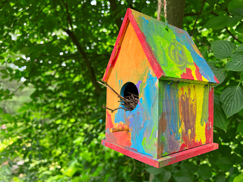 Small painted birdhouse on a string amongst some trees.