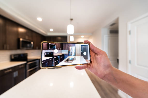 fotografía a mano de la casa apartamento cocina isla habitación en venta o alquiler con teléfono smartphone primer plano punto de vista en moderno condominio de lujo home tour con fondo bokeh borroso - visita fotografías e imágenes de stock