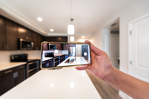 Hand photographing house apartment kitchen island room for sale or rent with phone smartphone closeup point of view in modern luxury condo home tour with blurry bokeh background