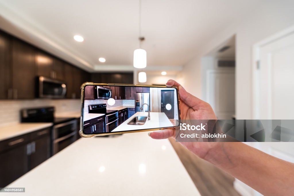Hand photographing house apartment kitchen island room for sale or rent with phone smartphone closeup point of view in modern luxury condo home tour with blurry bokeh background Hand photographing house apartment kitchen island room for sale or rent tour with phone smartphone closeup point of view in modern luxury condo home with blurry bokeh background Virtual Event Stock Photo