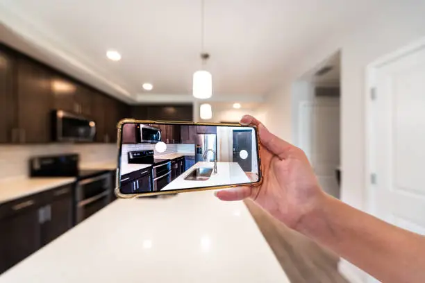 Hand photographing house apartment kitchen island room for sale or rent tour with phone smartphone closeup point of view in modern luxury condo home with blurry bokeh background
