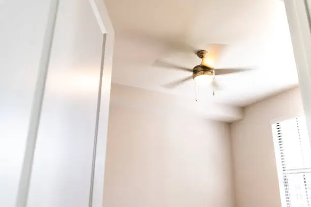 Empty bedroom room interior nobody looking up at lit illuminated yellow light spinning blurred motion ceiling fan open door window in new modern luxury apartment home house