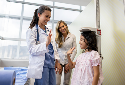 Happy pediatrician giving a high-five to a girl after measuring her height and seeing how much she has grown