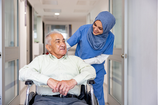 Happy Muslim nurse taking care of a senior patient leaving the hospital in a wheelchair - healthcare and medicine concepts