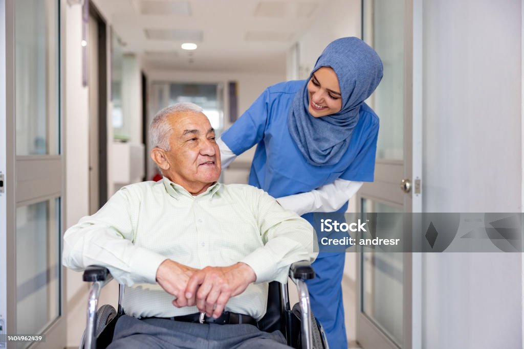 Muslim nurse taking care of a senior patient in a wheelchair Happy Muslim nurse taking care of a senior patient leaving the hospital in a wheelchair - healthcare and medicine concepts Nurse Stock Photo