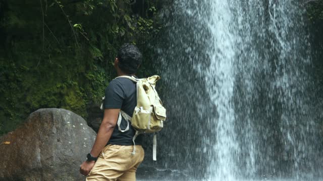 man walking  across a rocky surface to get to a waterfall in the forest
