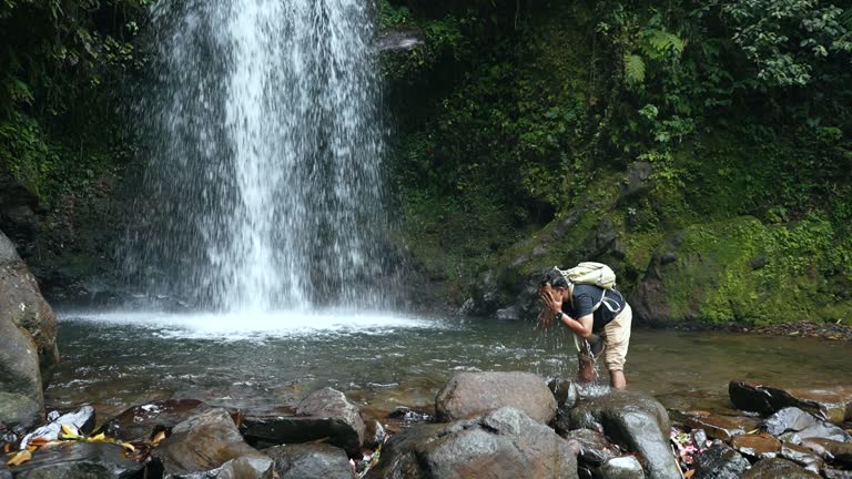 man walking  across a rocky surface to get to a waterfall in the forest