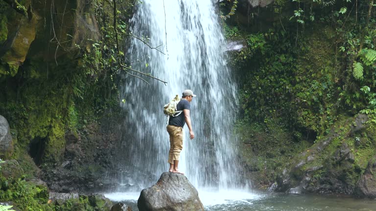 man walking  across a rocky surface to get to a waterfall in the forest