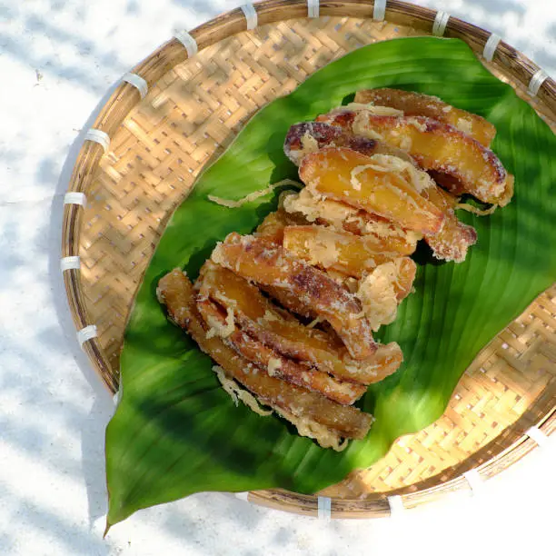 Bamboo tray of homemade food for snack diet, sliced yellow sweet potato that dried by sun exposure after marinated with sugar and ginger in hot day, Vietnam