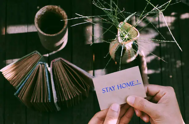 Top view outdoor table at morning with woman hand hold a piece of paper with STAY HOME message in epidemic season by corona virus, notebook, pencil ready for work at home in social quarantine period