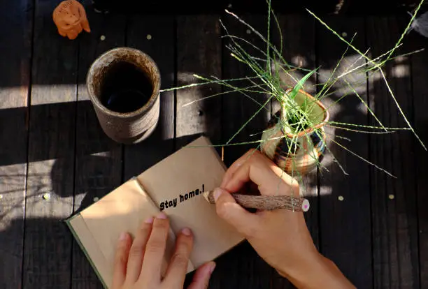 Top view outdoor table at morning with woman hand hold a piece of paper with STAY HOME message in epidemic season by corona virus, notebook, pencil ready for work at home in social quarantine period