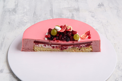 An angle shot of the half of a berry mouse pink cake decorated with berries on a tray.