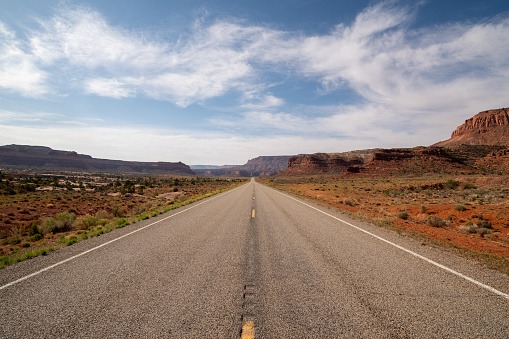 Straight desert road with yellow dividing lines seen at Arches National Park in the Southwest USA a hot summer morning.