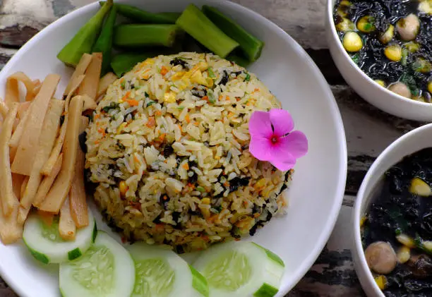 Top view plate of fried rice dish with vegetables as cucumber, bamboo shoot, okra and seaweed soup for family meal at lunch, delicious vegan food ready to eat on wooden background