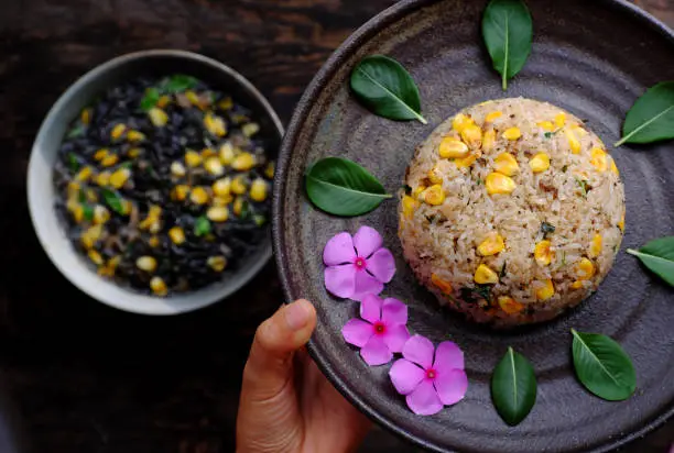Top view plate of Vietnamese vegan fried rice with yellow corn on dark background, woman hand hold delicious homemade vegetarian food ready to eat