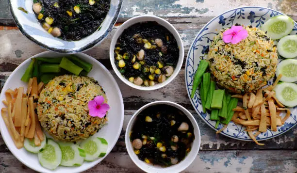 Top view two plate of fried rice dish with vegetables as cucumber, bamboo shoot, okra and seaweed soup for family meal at lunch, delicious vegan food ready to eat on wooden background