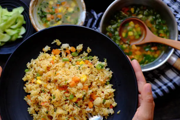 High view woman hand prepare food for quick dinner, Vegan meal with pilaw fried rice with soup from vegetables as carrot, corn, string bean, vegetarian dish in yellow, delicious Vietnamese cuisine