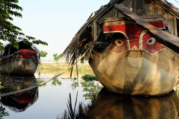 HO CHI MINH CITY, VIET NAM- JAN 15, 2020: Amazing wooden boat with dried leaves roof mooring at river, close up boat eyes looking straight, the boat reflect on water make impression art, Vietnam.