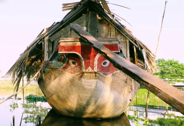 HO CHI MINH CITY, VIET NAM- JAN 15, 2020: Amazing wooden boat with dried leaves roof mooring at river, close up boat eyes looking straight, the boat reflect on water make impression art, Vietnam.