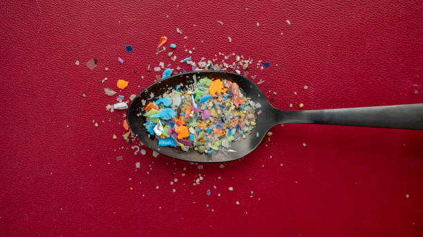 A pile of microplastics gathered from the beach in a spoon against a dark red background. Concept of global warming and climate change. Non-recyclable plastic pollution in the oceans. microplastic stock pictures, royalty-free photos & images