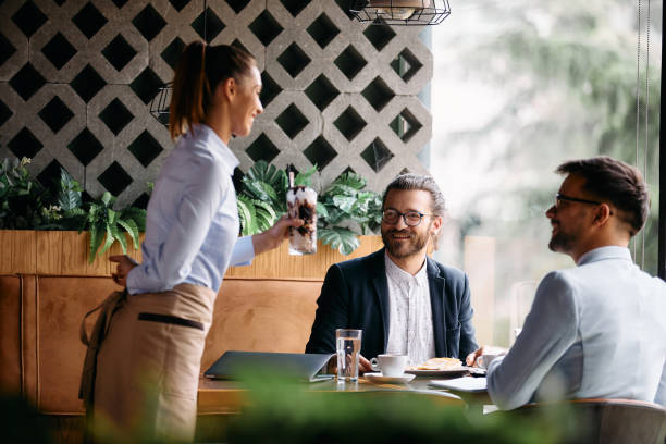 istock Young businessmen talking to a waitress while she is serving them coffee in cafe. 1404991002