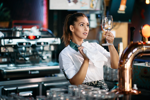 Female barista cleaning wine glass after work at bar counter.
