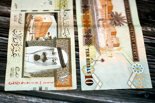 Saudi Arabia 10 SAR ten Saudi riyals cash money banknote with the photo of king Abdullah, Murabba palace and king AbdulAziz historical center isolated on a wooden background, selective focus