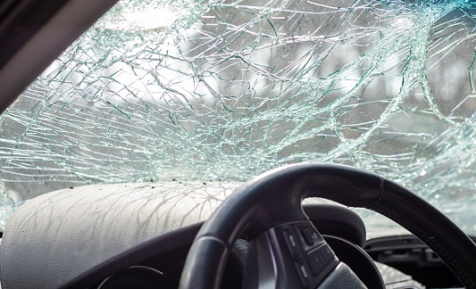 Damaged car window after an accident. Broken windshield as a result of an accident, inside view. Cabin interior details, view from the cab. Safe movement. Broken windshield. Glass crack and damage