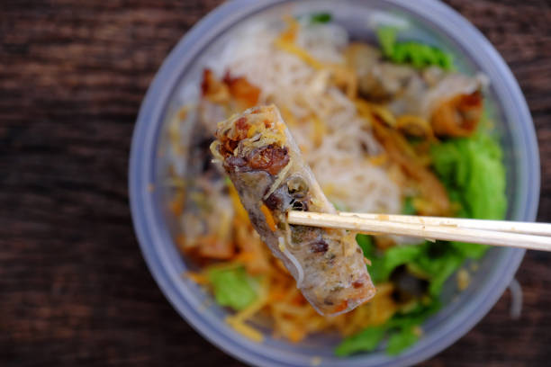 istock hand hold chopsticks pick up fried spring rolls on vegan rice noodles 1404999038