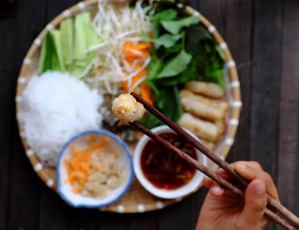 people hold chopsticks pick up fried spring rolls on tray of Vietnamese vegan food, rice noodle with rolls, popular Vietnam cuisine