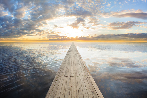 Wooden bridge on the sea which has walk way for travel with beautiful sky and sunshine background.