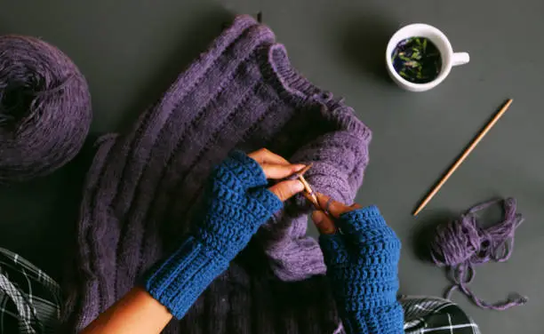 Photo of woman hand wear blue mitten crochet, knit violet sweater for gift on dark tone