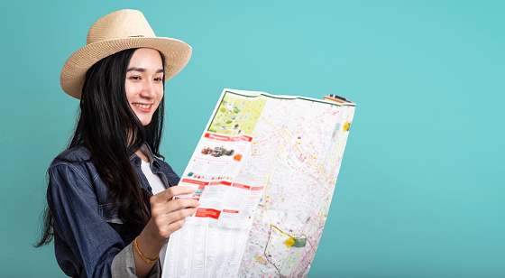 Happy smiling tourist asian woman in summer on a trip with map isolated on blue background , Female asia traveling hold city map