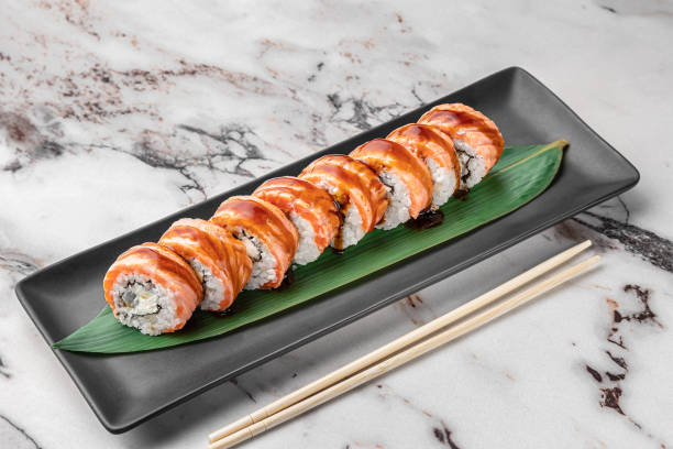 istock set of maki rolls with smoked eel and green bamboo leaf in a black ceramic plate with chopstick on a bright white textured marble background, side view 1405003842