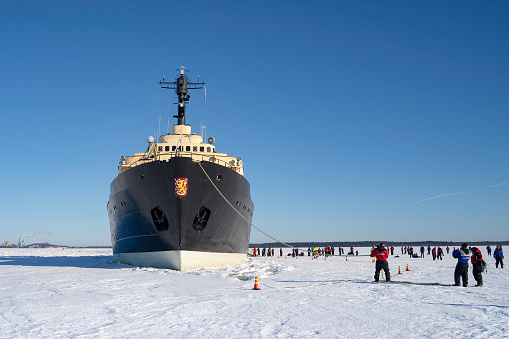 Rovaniemi, Finland - March 21st, 2022: Sampo, an icebreaker ship, anchored on the frozen baltic sea, on a sunny winter day, tourists on the icy surface beside it.