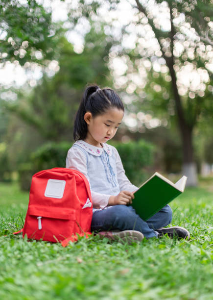 istock Little Girl Reading Book on Grass 1405007815