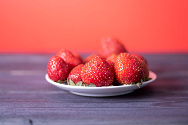 Fresh strawberries in a white plate on a dark wooden background. The concept of fresh and healthy food.