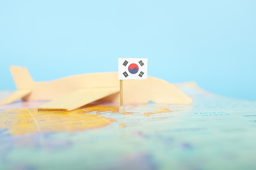 Selective focus of South Korean flag in blurry world map and wooden airplane model. South Korea as travel and tourism destination concept.