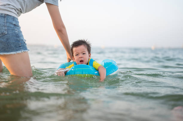 милый мальчик плавает на берегу моря с поплавком с мамой - water sport family inner tube sport стоковые фото и изображения