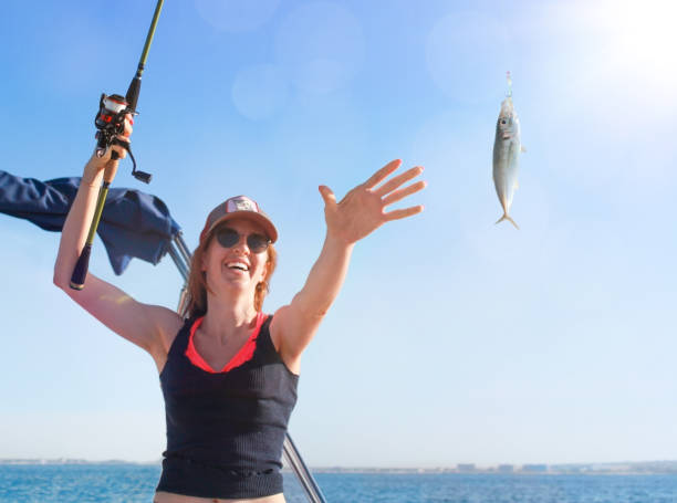 the hand of a young girl reaches for a caught fish on a fishing rod. the girl is very happy that she caught a fish - recreational boat nautical vessel fishing rod motorboat imagens e fotografias de stock