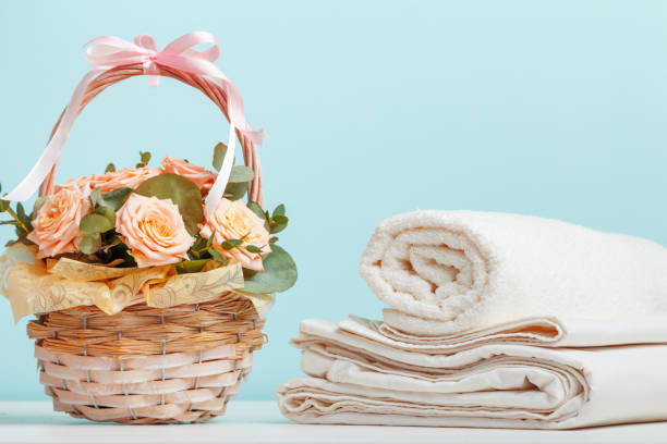 istock White bed linen sheets roll towels basket with flowers on the table on a blue background. 1405022833