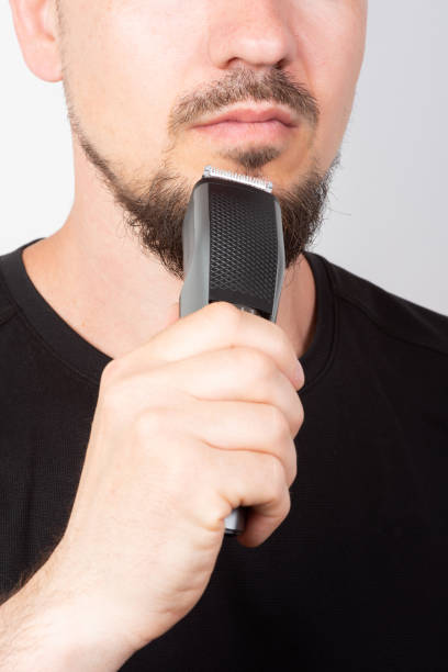 istock man shaving his beard with a trimmer, close-up 1405023608