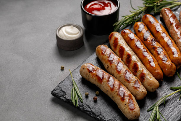 Grilled assorted sausages with sauces and rosemary. Homemade sausages on a stone board. Grilled assorted sausages with sauces and rosemary. Homemade sausages on a stone board. Dark background. Copy space. bratwurst stock pictures, royalty-free photos & images