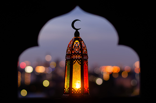 Linterna que tiene símbolo de luna en la parte superior con enfoque borroso de papel cortado para fondo de forma de mezquita. photo