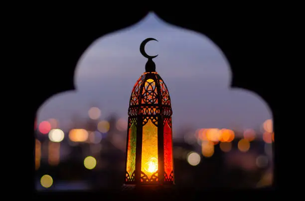 Lantern that have moon symbol on top with blurred focus of paper cut for mosque shape background. Ramadan Kareem and Islamic new year concept.